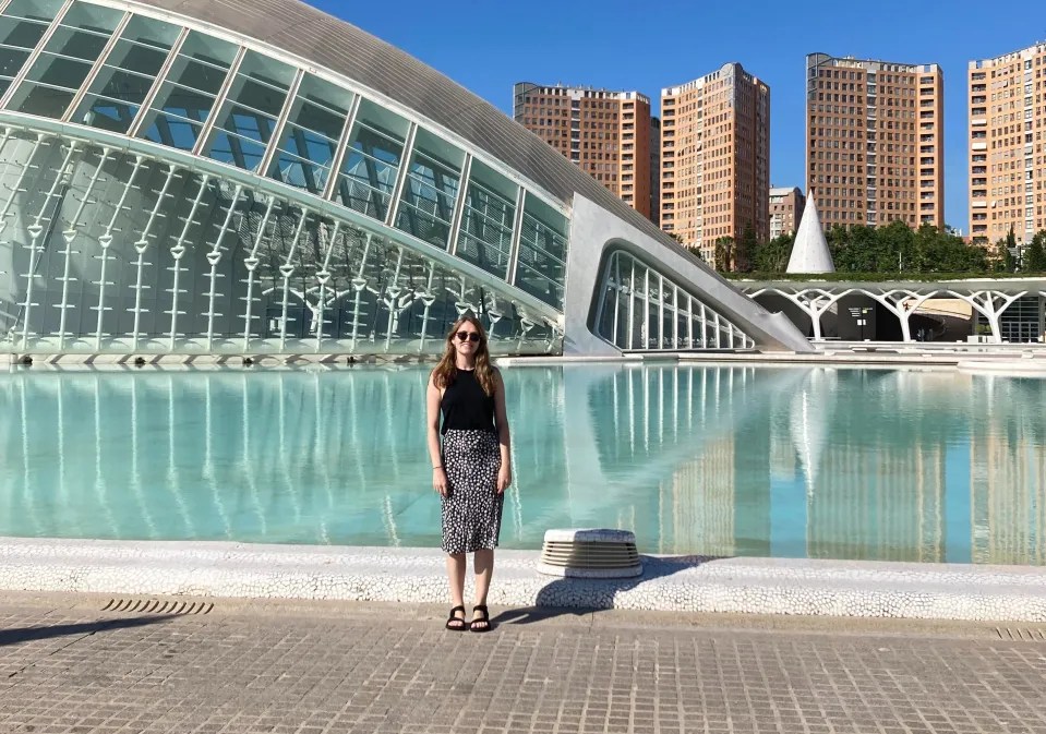 Woman standing in front of a modern building and reflecting pool.
