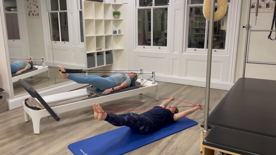 Two women performing Pilates exercises using resistance bands and a reformer machine.