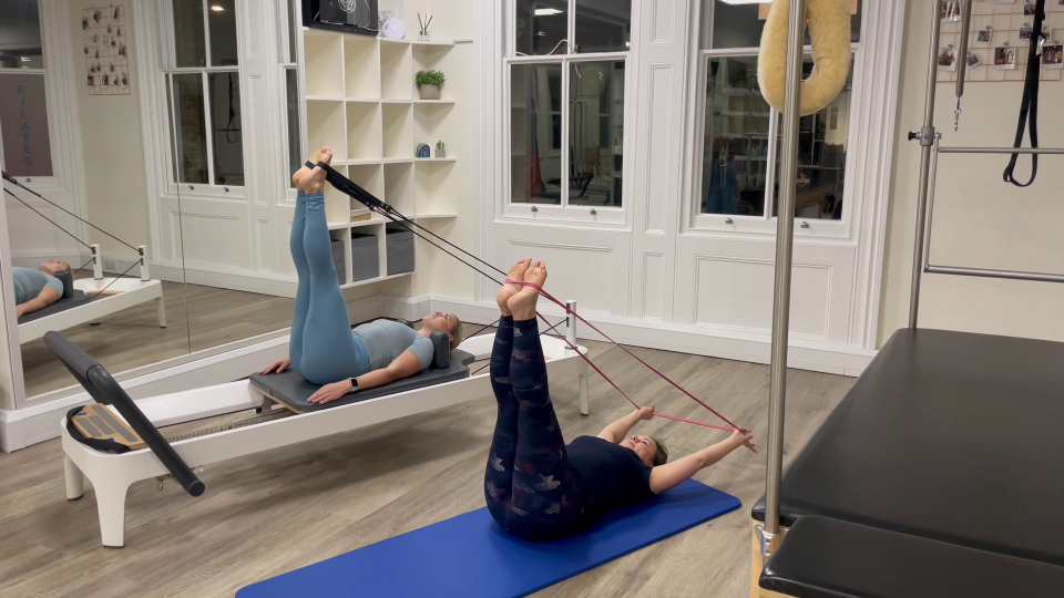 Two women performing Pilates exercises using resistance bands.