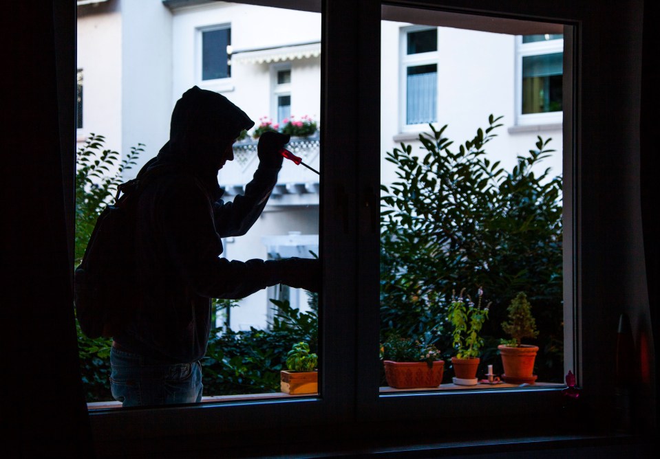 Silhouette of a burglar using a screwdriver to break into an apartment through a window.