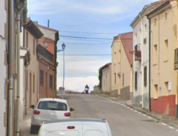 Street scene with parked cars and a person on a scooter going uphill.