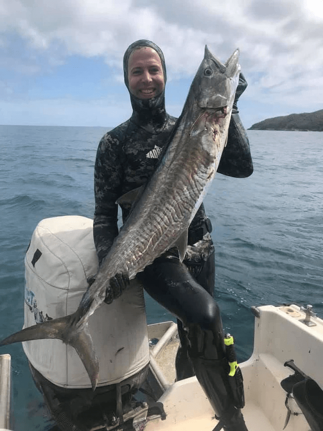 Spearfisherman holding a large fish on a boat.