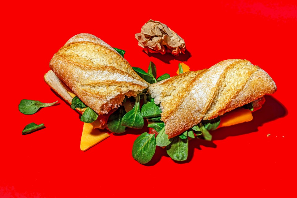 Half-eaten sandwich with cheese and lettuce on a red background.
