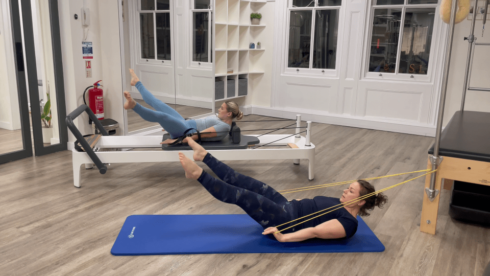 Two women performing Pilates exercises using resistance bands.