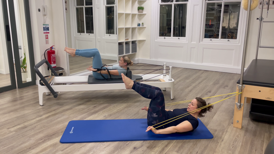 Two women performing Pilates exercises using resistance bands.