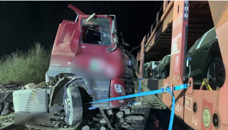 Damaged semi-truck attached to a train car carrying new cars.