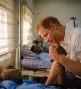 Prince Harry holding a patient's hand in a hospital.