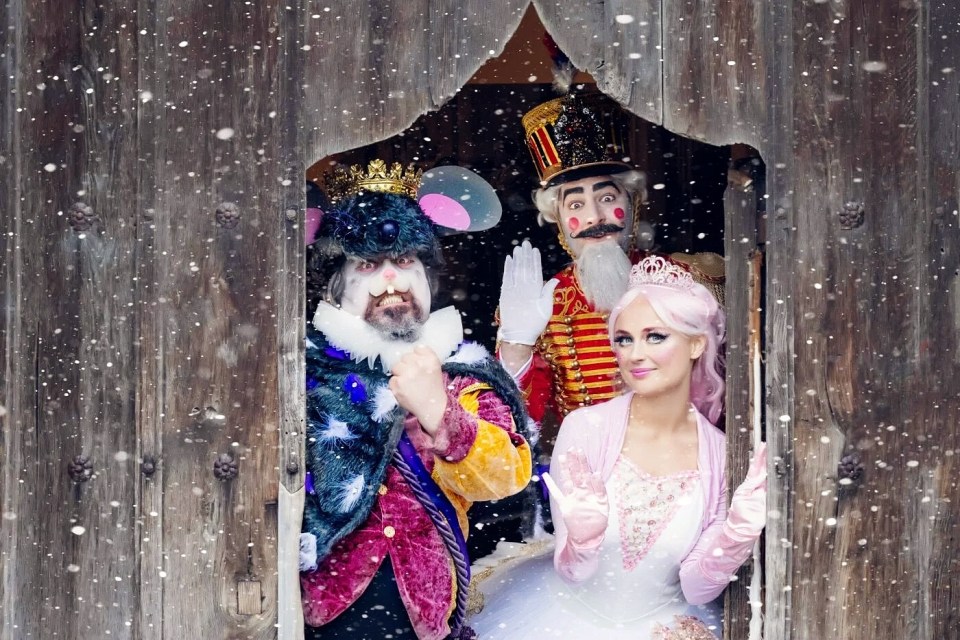 Three people in Nutcracker costumes appear in a doorway during a snowfall.