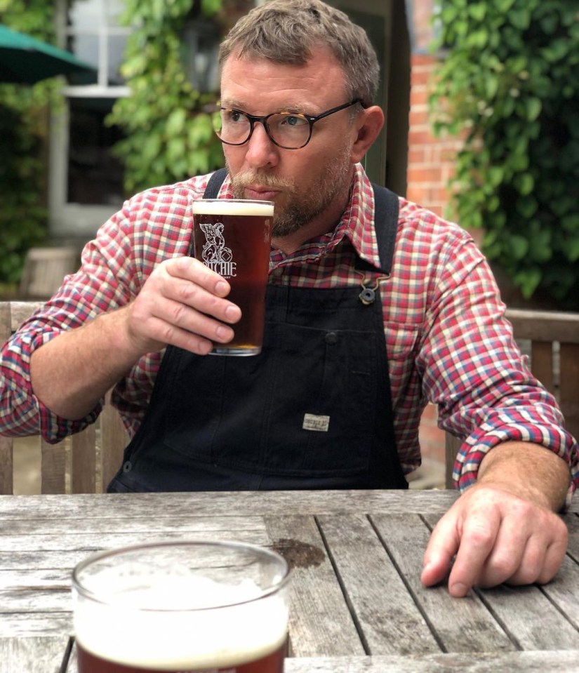 Guy Ritchie drinking beer outdoors.