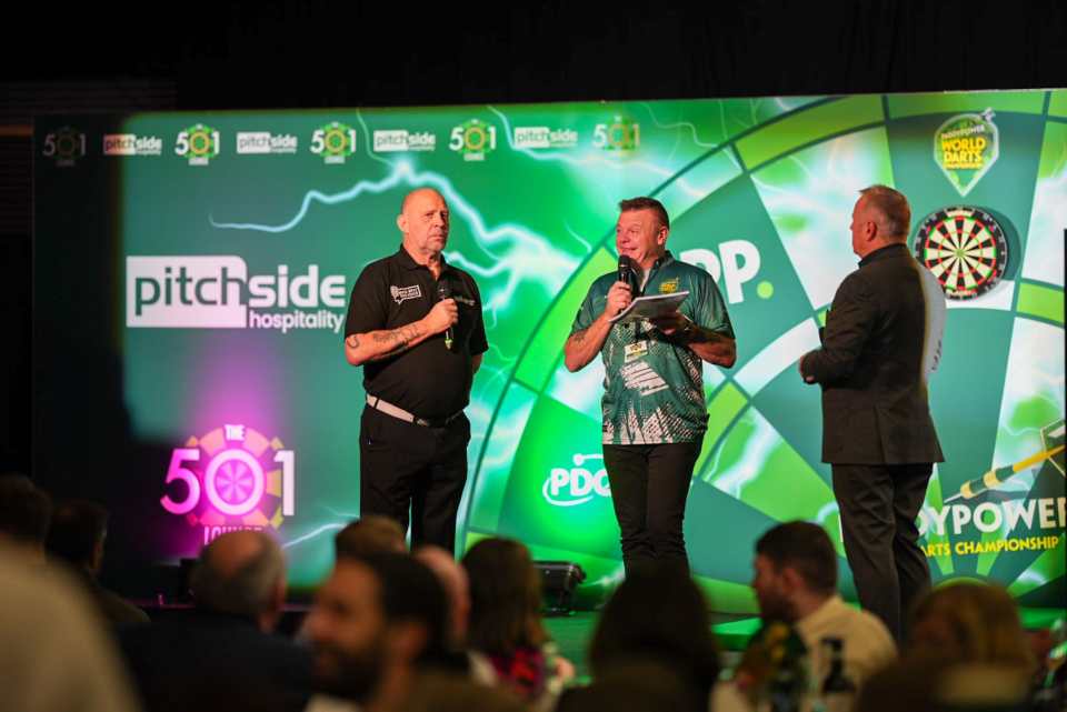 Two men speaking at a darts championship event.