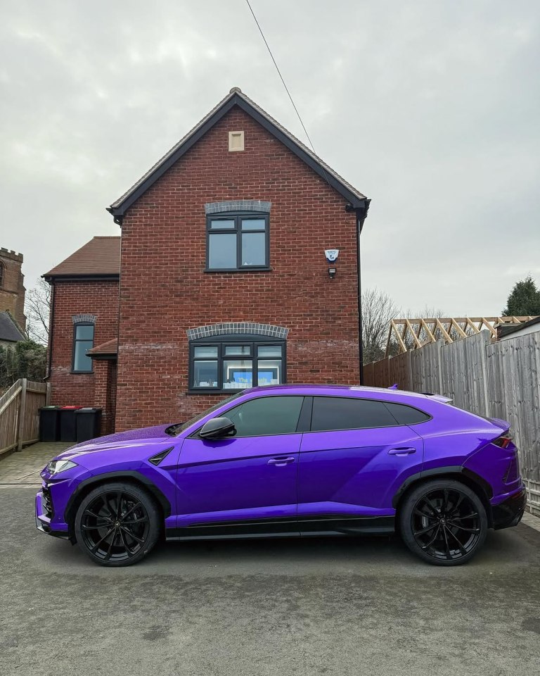Purple Lamborghini Urus parked in front of a brick house.