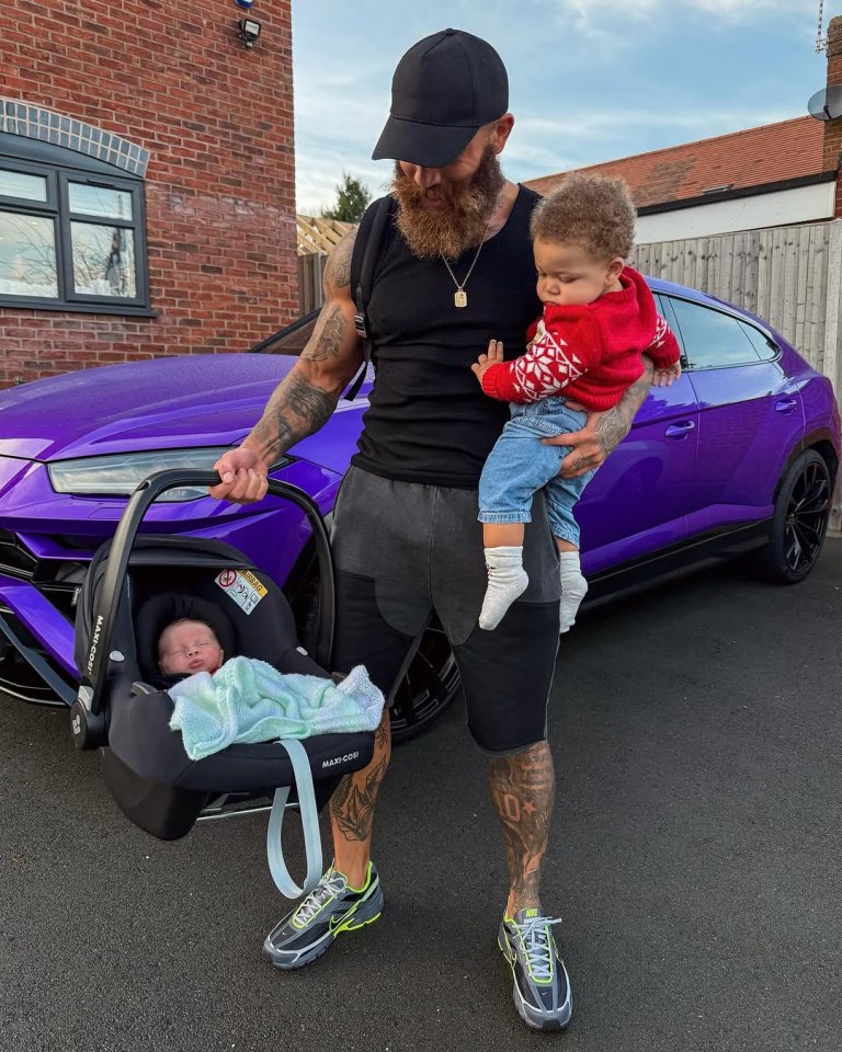 Man holding two babies near a purple car.