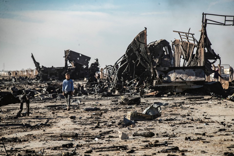 Boy walking past destroyed military vehicles.
