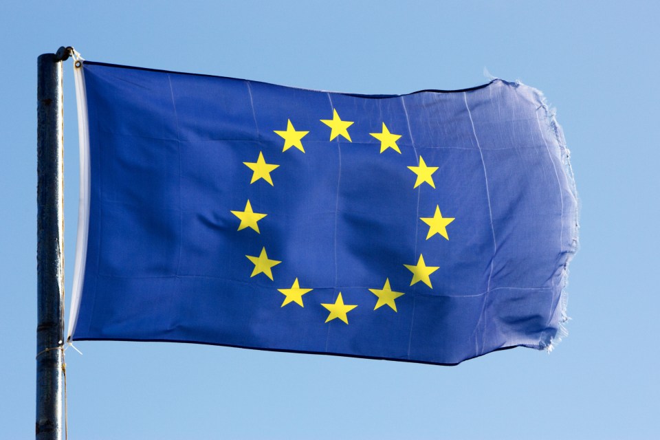 A tattered European Union flag flies against a clear blue sky.