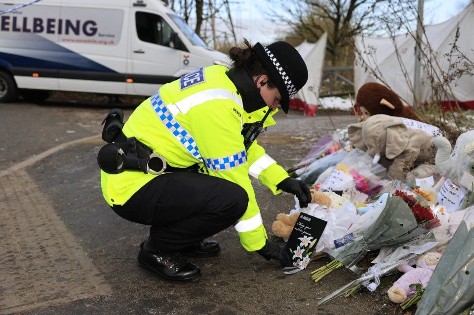 Police officer placing a tribute among flowers and stuffed animals left for baby Ava.