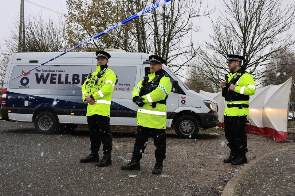 Three police officers stand at a crime scene in snowy weather.