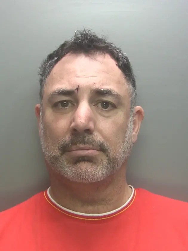 Mugshot of a man with graying hair and a red shirt.