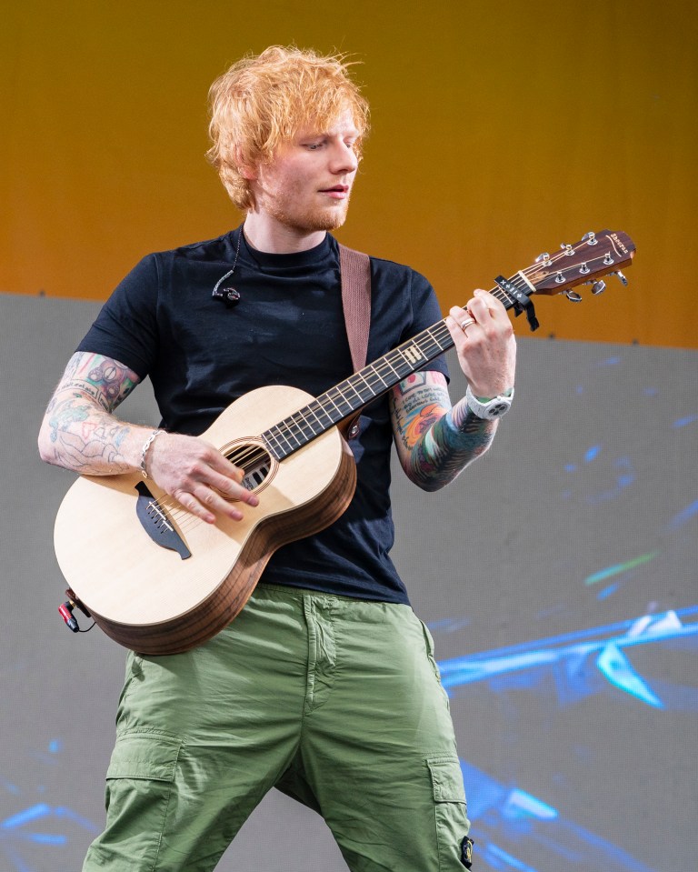 Ed Sheeran performing at a music festival, playing an acoustic guitar.