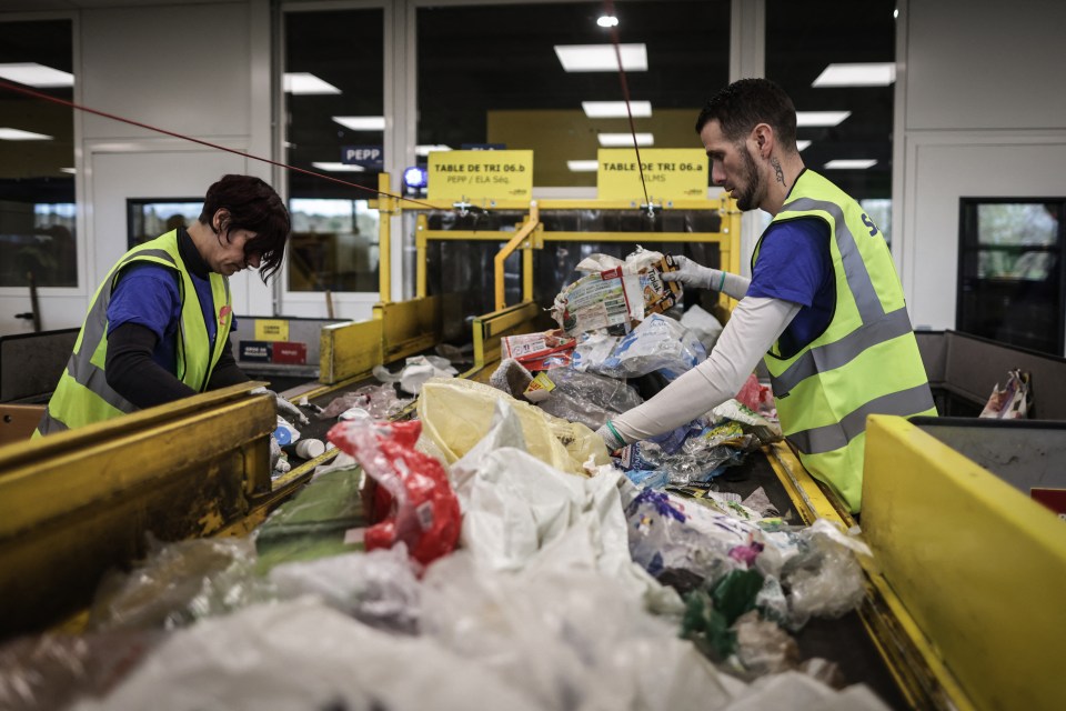 Workers manually sort plastic waste on a conveyor belt.
