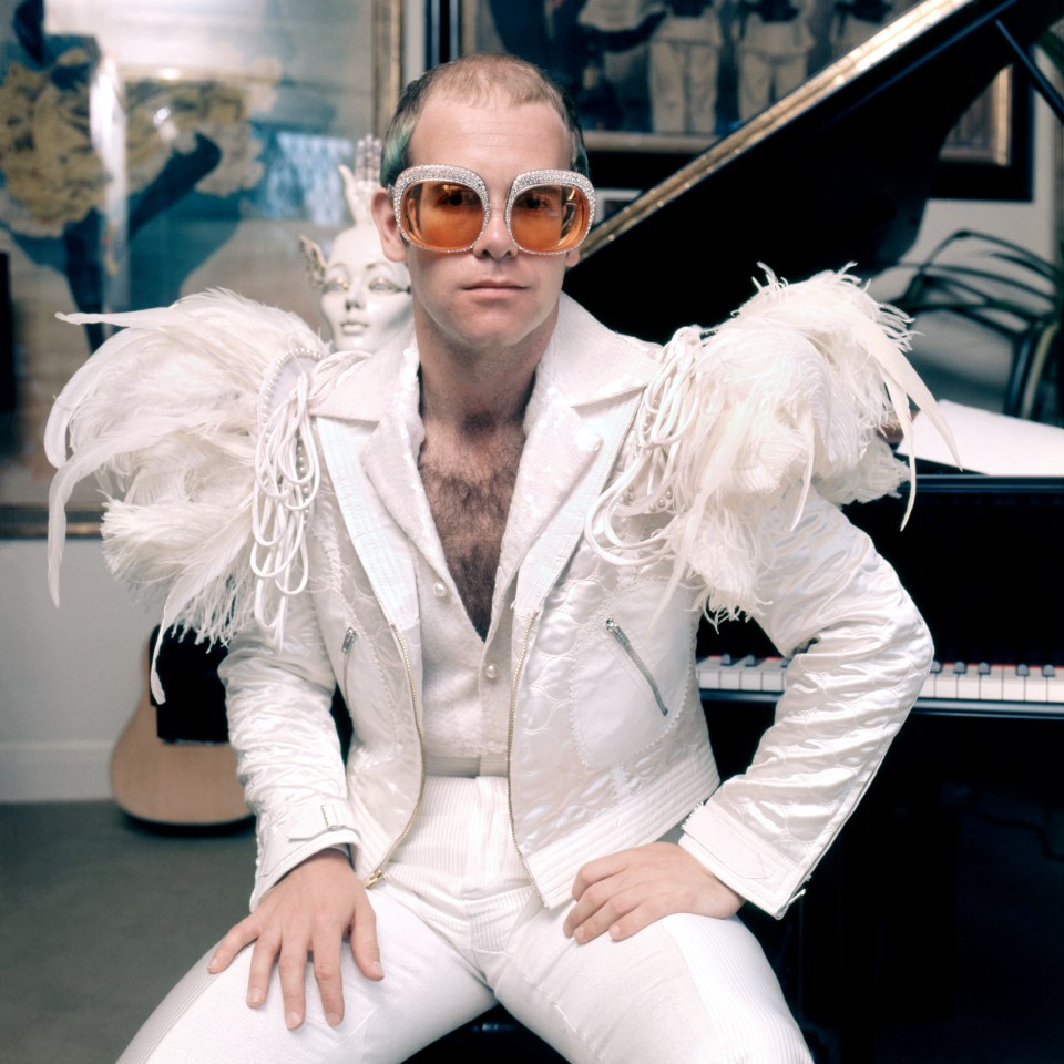 Elton John in a white feather-trimmed suit and rhinestone glasses.