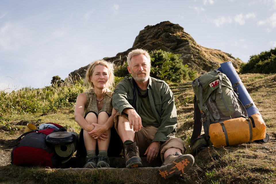 Gillian Anderson and Jason Isaacs resting on a hike.