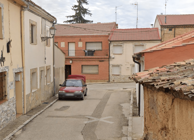 Red car parked on a narrow street between old buildings.