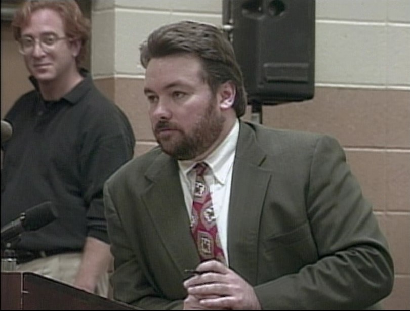 Man in suit speaks at podium.