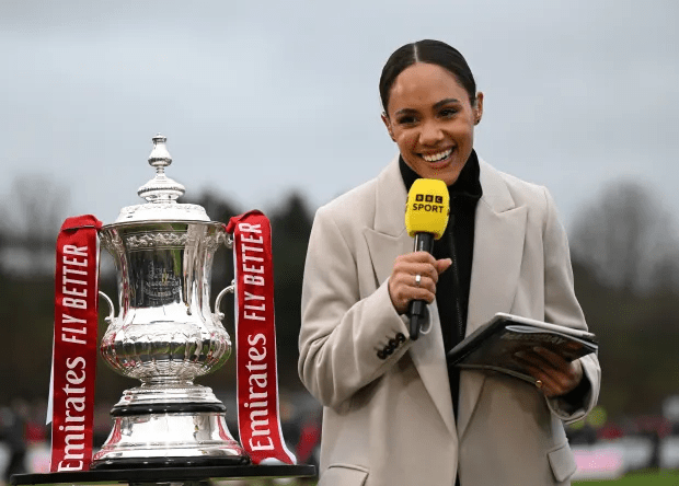 A woman holding a BBC Sport microphone stands in front of a trophy with "Emirates Fly Better" ribbons.