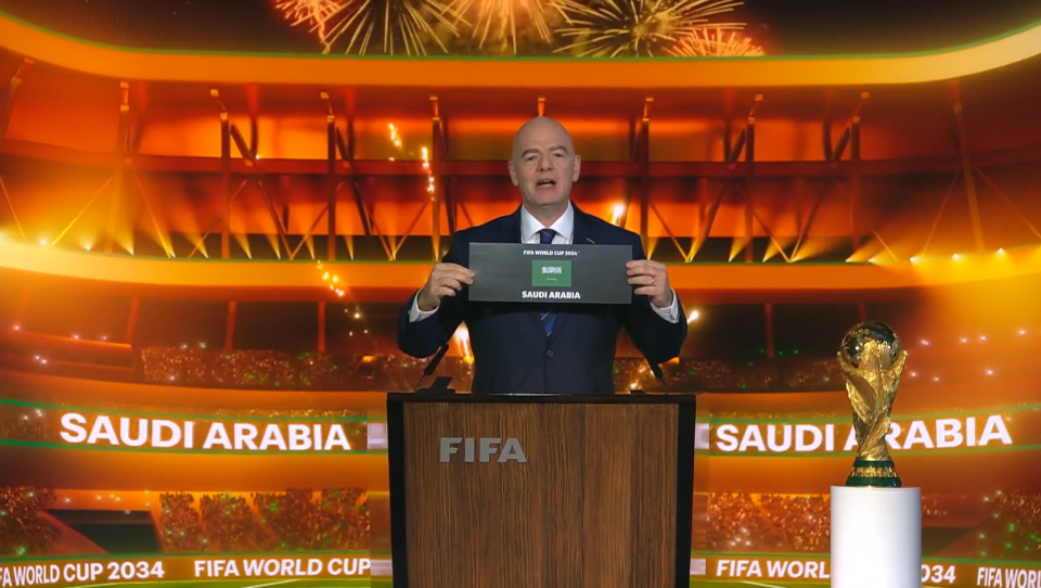 A man at a podium announces Saudi Arabia as the host of the 2034 FIFA World Cup.