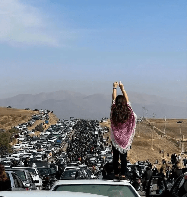 Woman standing on a car, arms raised, overlooking a massive traffic jam.