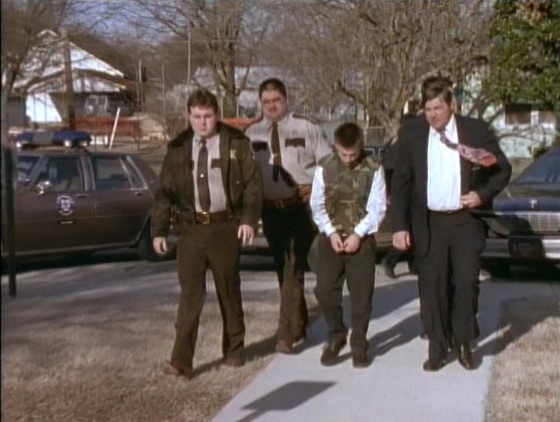 A handcuffed young man escorted by police officers.