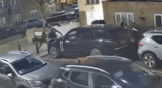 Nighttime surveillance footage of people tampering with a black SUV.