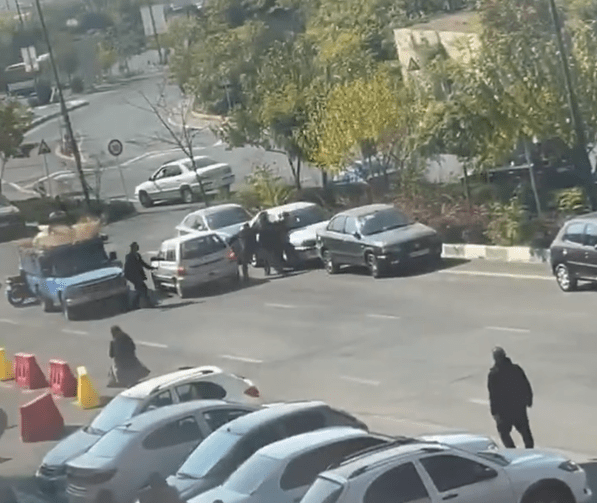 People standing in a street near parked cars.
