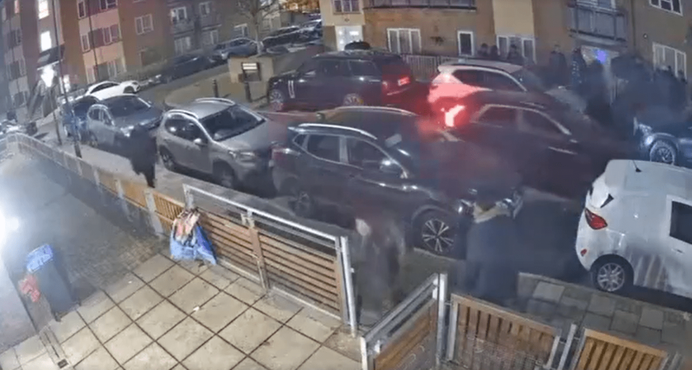 Nighttime security footage showing several cars parked on a residential street with a group of people standing nearby.