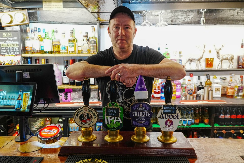 Pub landlord standing behind bar.