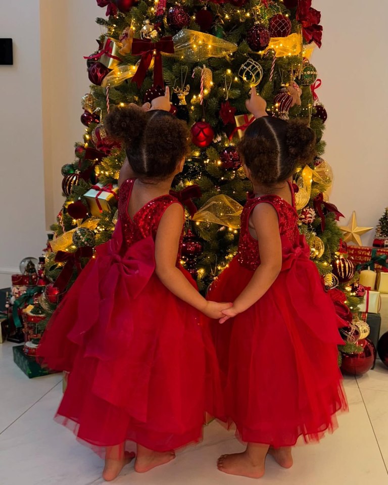 Twin girls in red dresses admiring a Christmas tree.