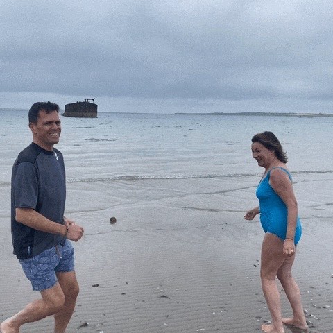 Lorraine Kelly and a companion in swimsuits on a beach.