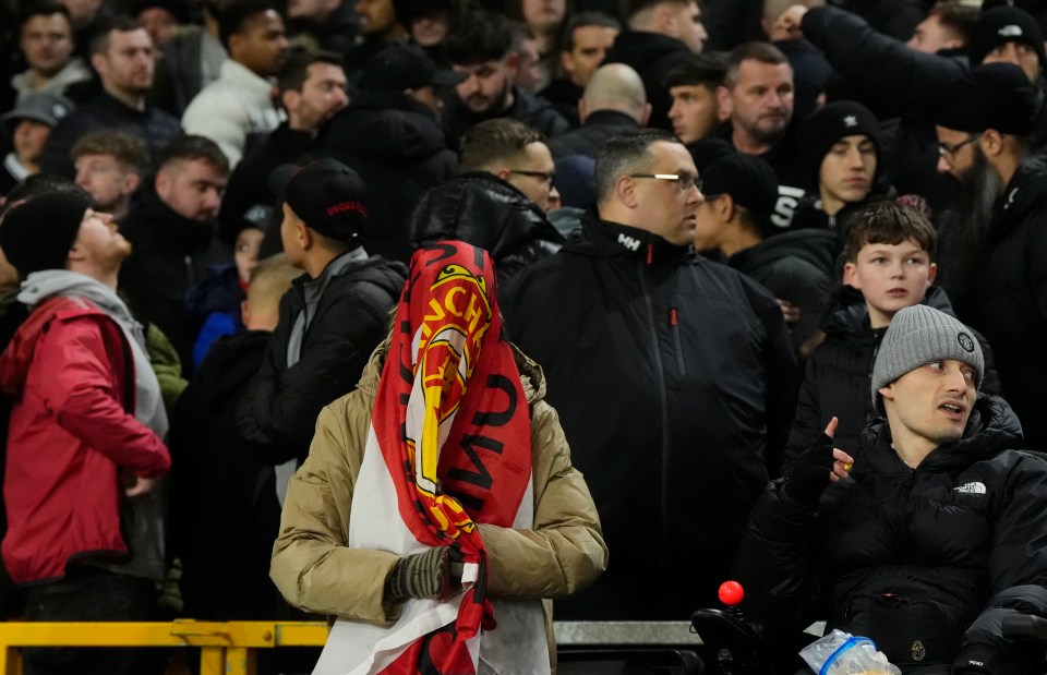 A Manchester United fan covers their face with a team flag at a match.