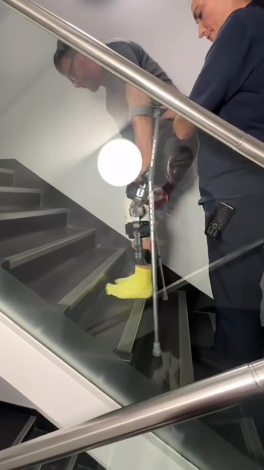 Man with leg brace and crutches ascending stairs with assistance.