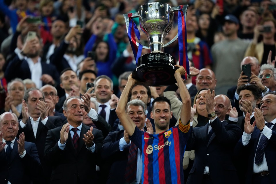 Sergio Busquets lifts the La Liga trophy with Luis Rubiales and other officials looking on.