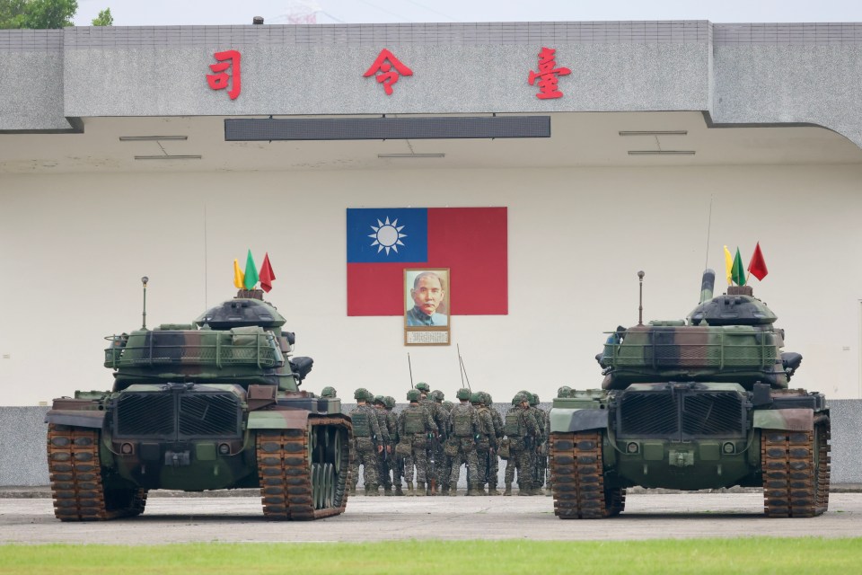 Taiwanese military personnel standing between two tanks in front of a building displaying the Taiwanese flag.