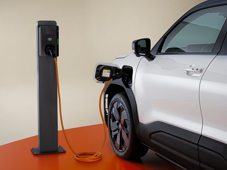 A white Toyota Urban Cruiser electric SUV charging at a charging station.
