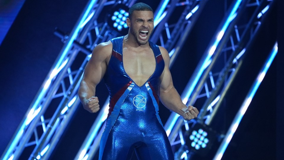 A muscular man in a blue and red leotard shouts with fists clenched.