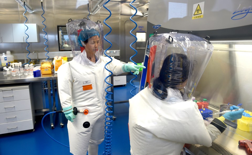 Two scientists in protective suits working in a lab.