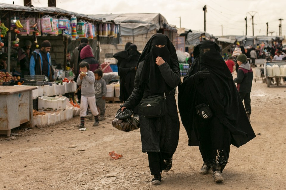 Two women in niqabs walk through a Syrian marketplace.