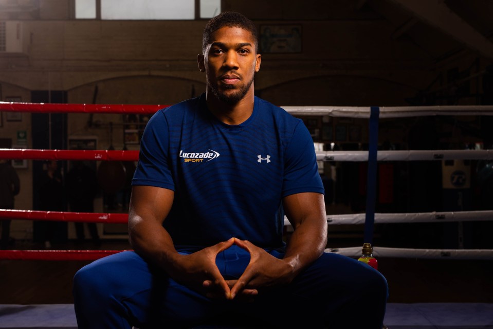 Anthony Joshua in a boxing gym, sitting and wearing a Lucozade Sport shirt.