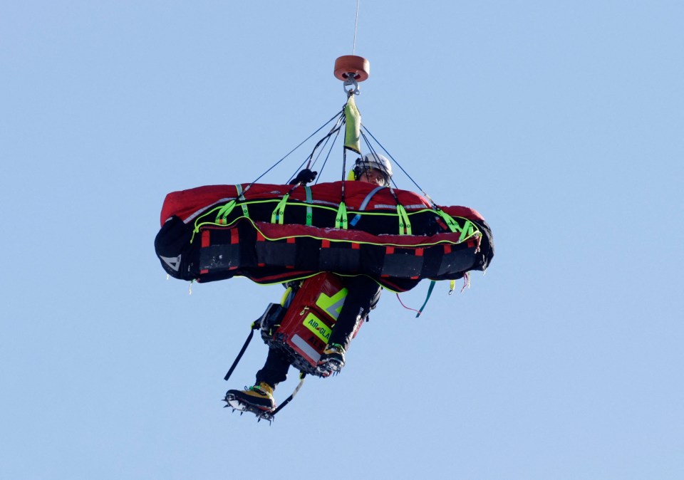 A skier being airlifted in a rescue stretcher.