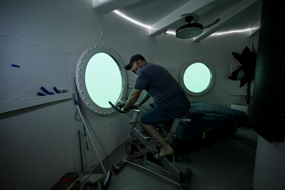 Man exercising on stationary bike in underwater room.