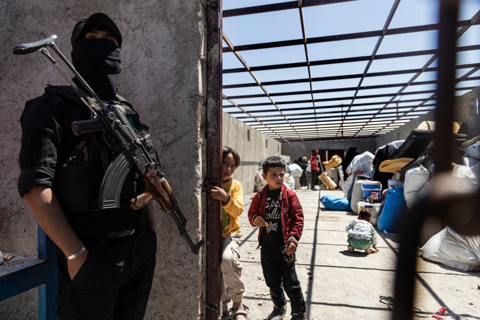 Syrian women and children leaving a camp, guarded by a SDF fighter.