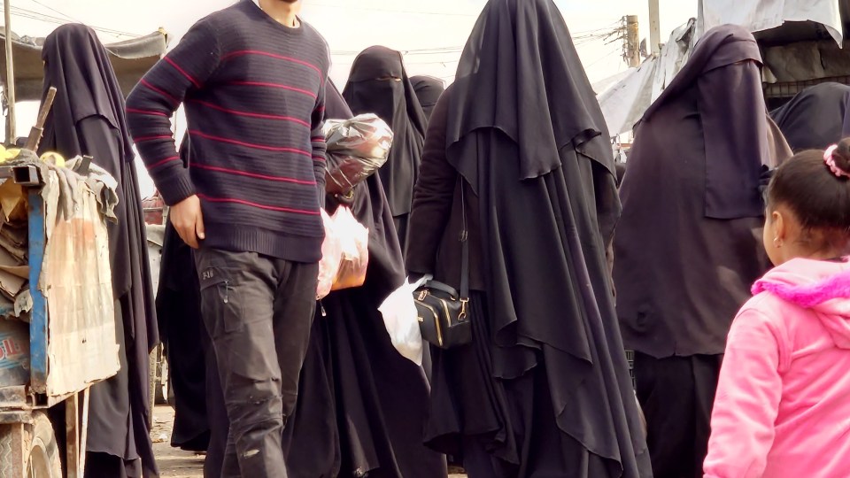 People in niqabs and abayas walking in a market.